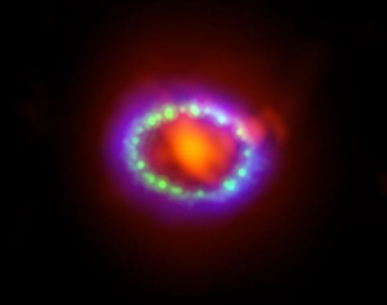 这张图像展示的是超新星SN 1987A在不同波段的观测结果合成效果。ALMA的数据(红色)展示的是爆发残骸中心部位新形成的尘埃云；哈勃的数据(绿色)以及钱德拉望远镜的数据(蓝色)则展示了不断向外扩张的冲击波。