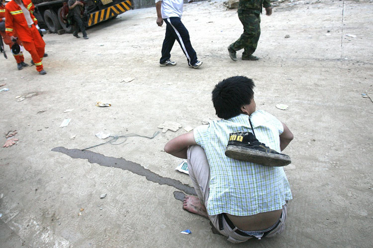 图文:因地震惊吓过度的男子背着鞋坐在路边