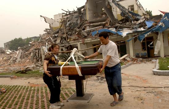2008年5月18日、漢旺鎮、二人の住民が廃墟の中から自家用麻雀卓を運び出している。麻雀は四川の人が最も愛する娯楽である。