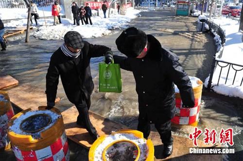 图为由于水管爆裂，流水将一处人行道阻断，抢修人员在此处搭建简易通道，一名警察搀扶老人。