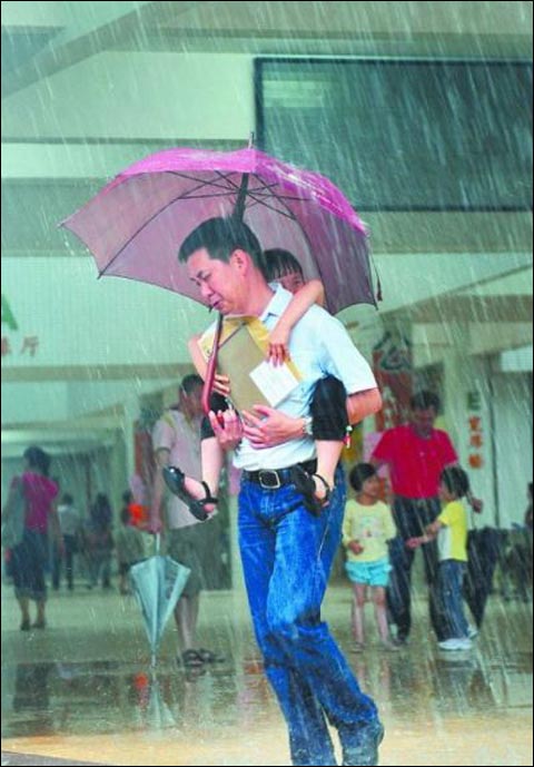 23日,中山市一位家长背着孩子在雨中艰难前行(图片来源:中山商报)