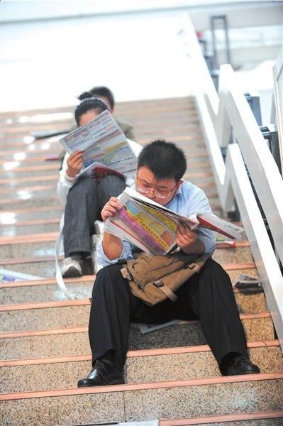 应聘者坐在楼梯上休息且看着相关招聘的报纸。本报记者朱嘉磊摄