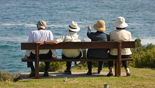 Two elderly couples sit on a bench and look out to sea