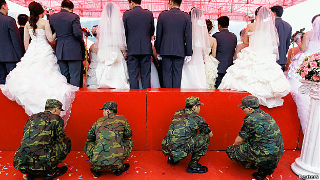 Soldiers crouch behind a platform as married couples pose for photos