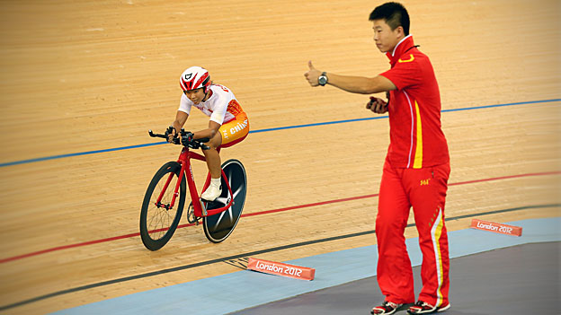 Sini Zeng of China cycles past her coach as he gives the thumbs up during the London 2012 Paralympic Games. 