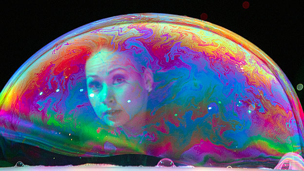 Bubble artist Melody Yang looks through a large bubble on a table. 