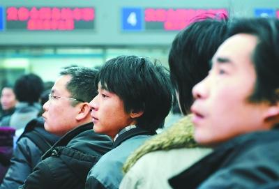 在车站排队买票的旅客在看大屏幕上显示的火车票信息