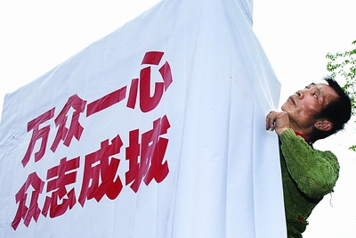 在安仁镇,村民正在将"万众一心,众志成城"的标语牌立在路边.