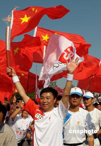 7月9日,奥运火炬在内蒙古鄂尔多斯传递,火炬手在高扬的旗帜下传递火炬